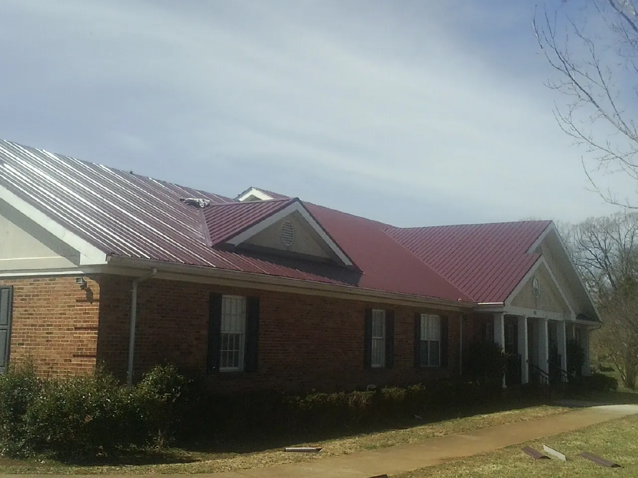 Red metal roof with gabled entries on a long brick building, from a Hail Damage Roof Repair job in Hamilton City