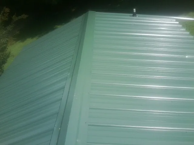 New green metal panels meeting at the ridge of a roof — Flat Roof Repair work by our crew in Hamilton City