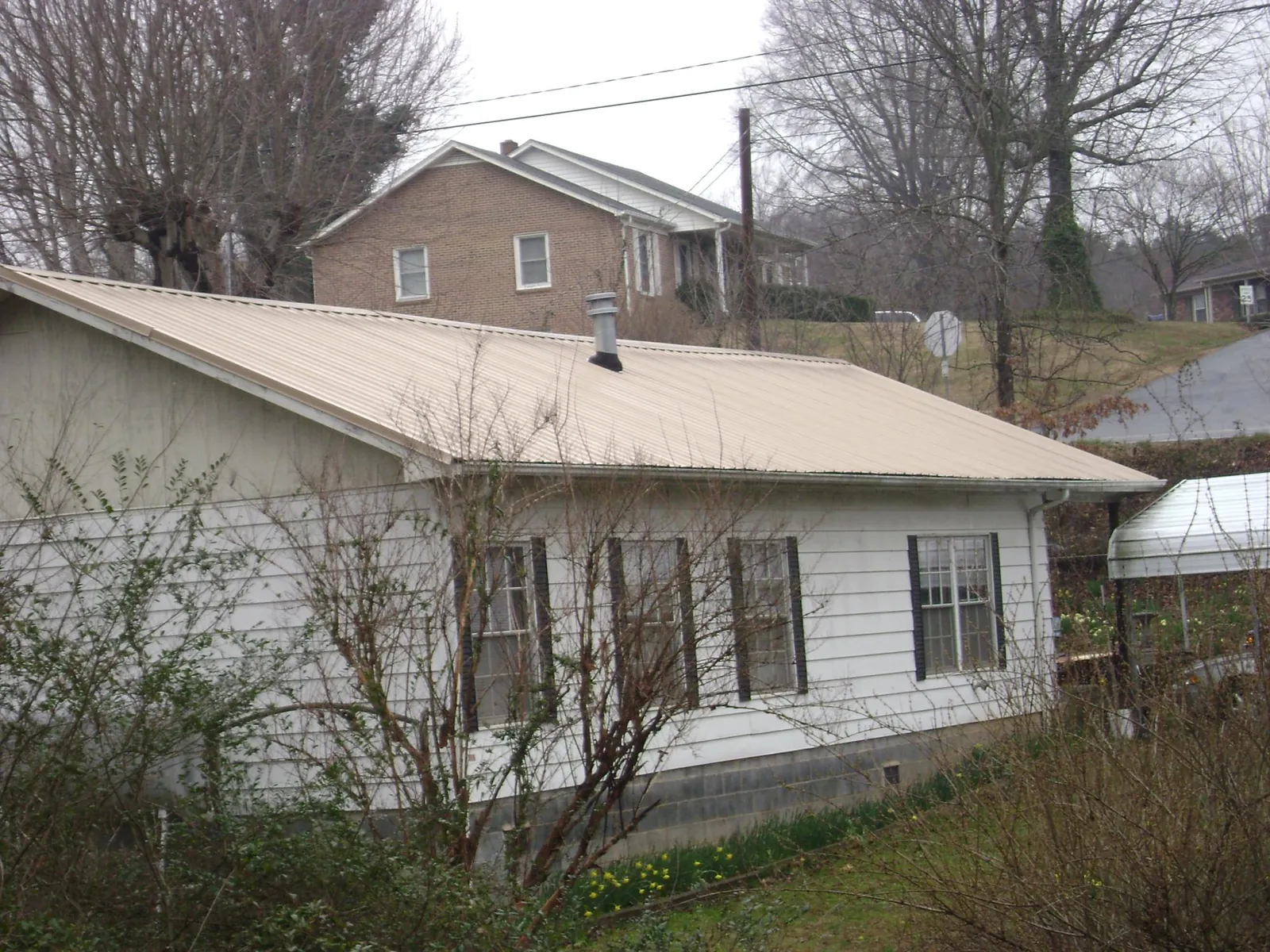 Tan metal roof on a white sided house set into a hillside — Commercial Roofing by Roofing Brothers in Hamilton City