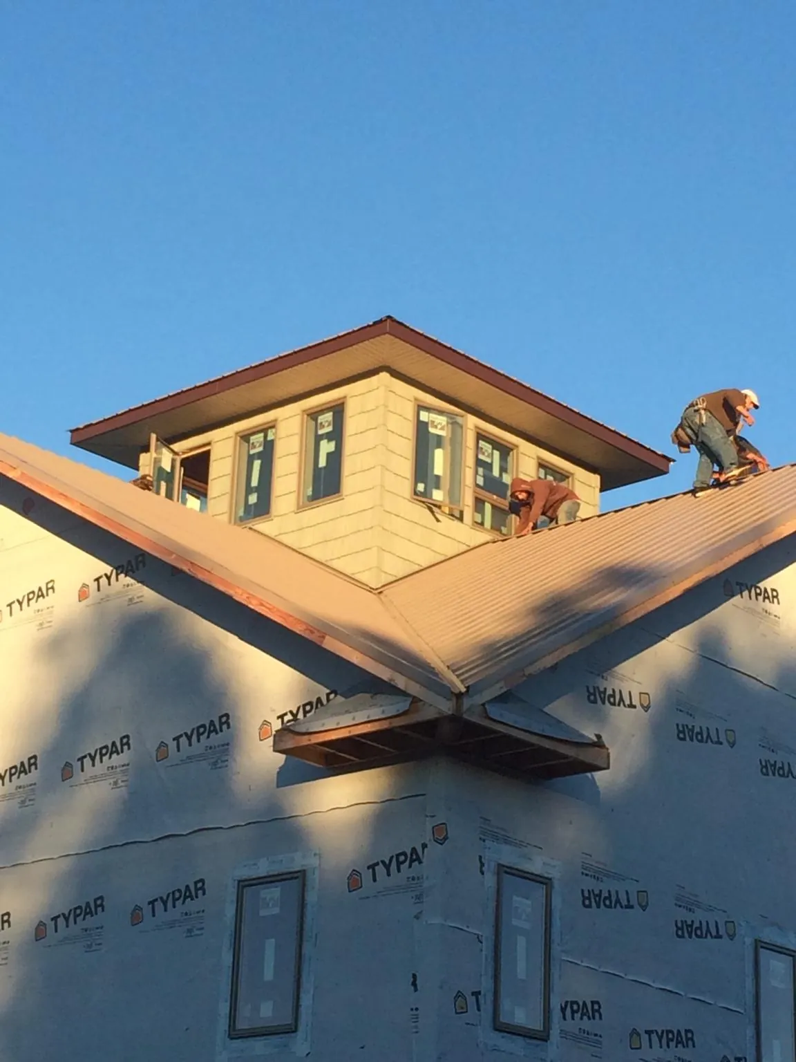 Roofers working around a rooftop cupola on a new metal roof at sunset — Roof Waterproofing in Hamilton City by Roofing Brothers
